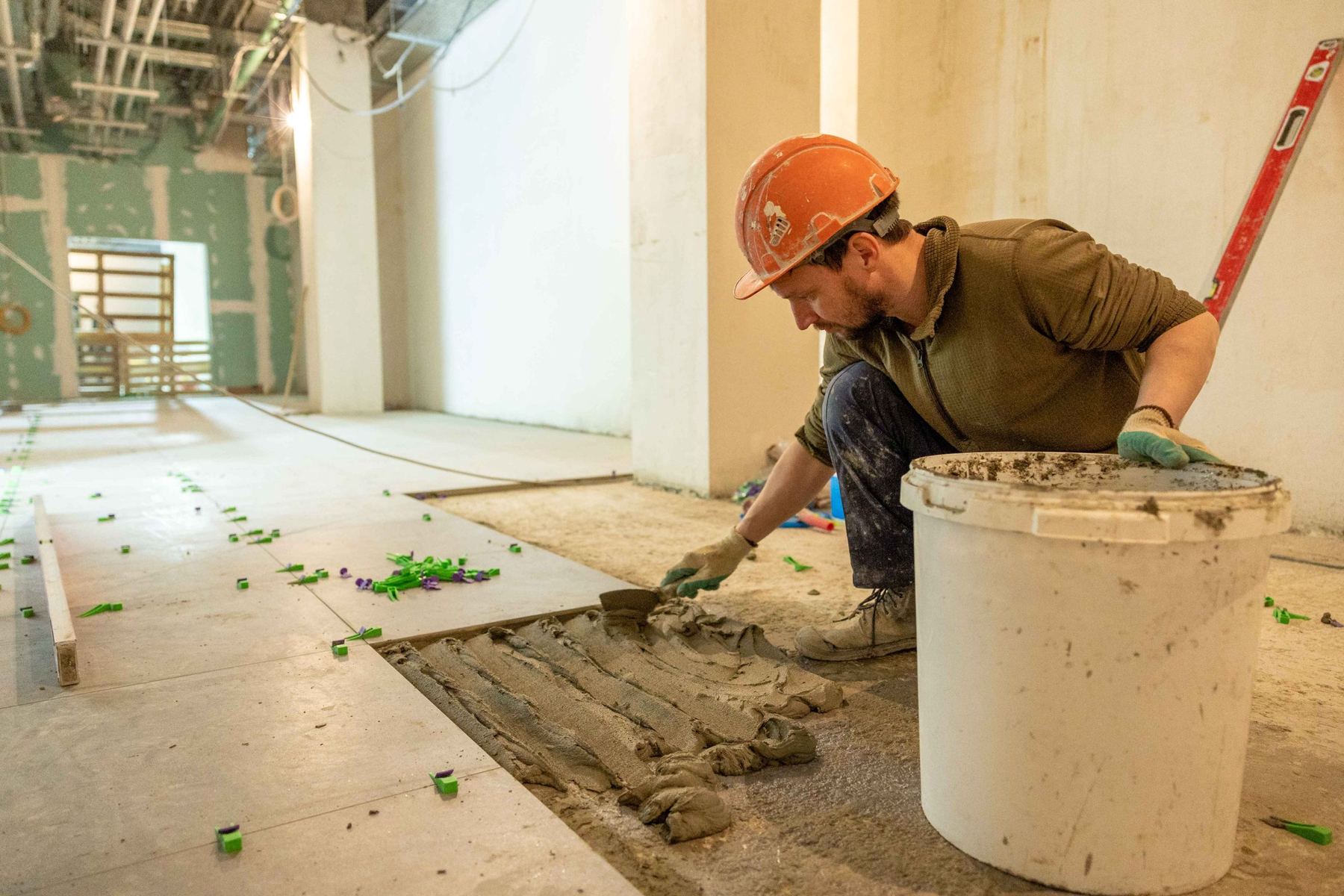 A tiler in a hard hat bedding floor tiles on site